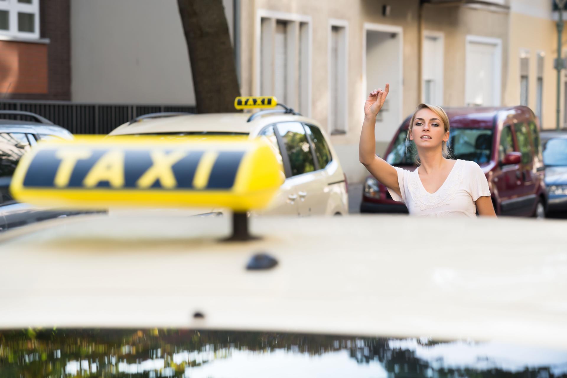 Woman Raising Arm To Hail Taxi On Street