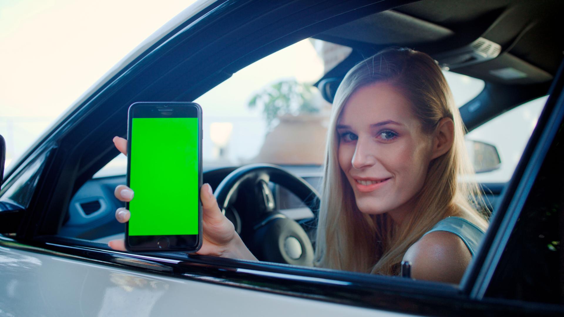 Female driver using digital vaccine passport app in mobile phone. Leaning out of the car window